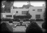 Irving Gill's Dodge House, a mid-century modern house. Black and white photo of the garden front, white stucco walls, a fabric awning over the terrace, and a decorative pool with water plants and fountain.