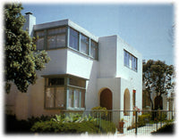 Color photo of Horatio West apartments in Santa Monica by Irving Gill. White stucco walls with green painted window frames, flat roofs